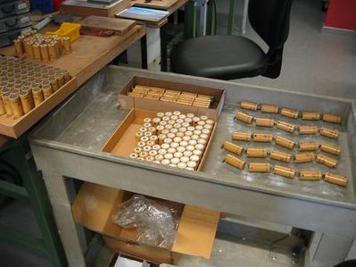 lose Stränge
In der Mitte des Rolltisches die Zellen auf der Lieferpalette, rechts davon lose 5er Stränge, links auf dem Tisch bereits mit einer Lötfahne vorbereitete Zellen auf Palette.
